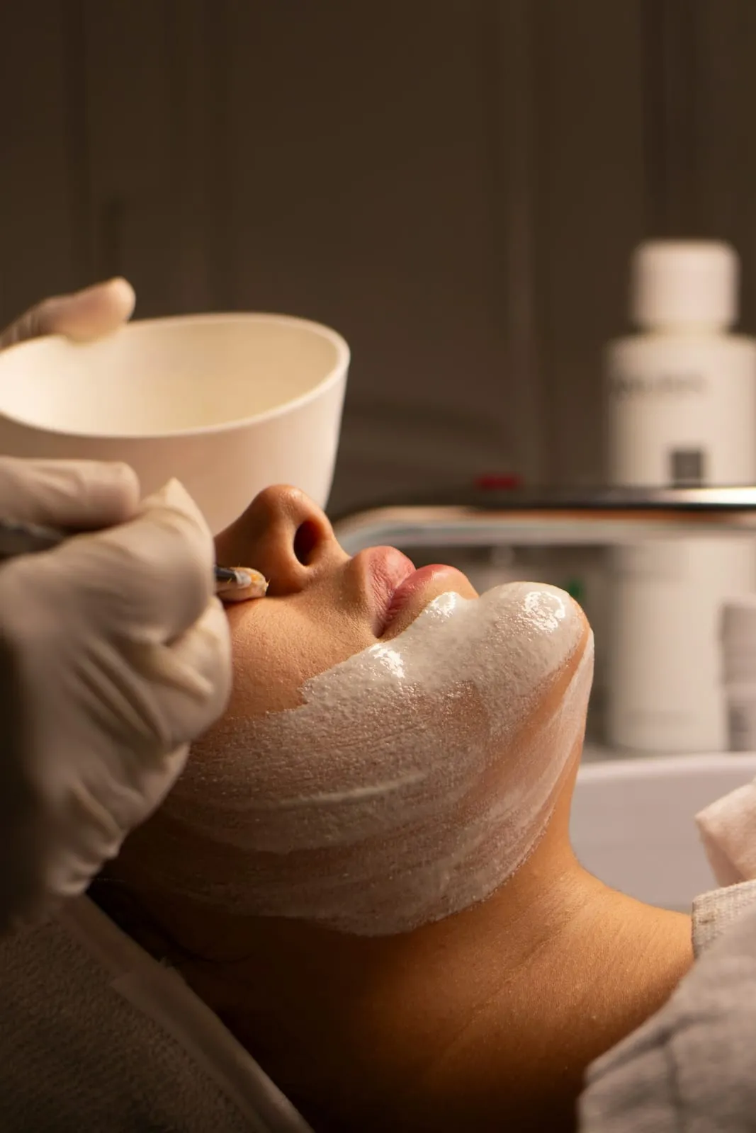 A therapist in gloves applying a cream face mask during a facial